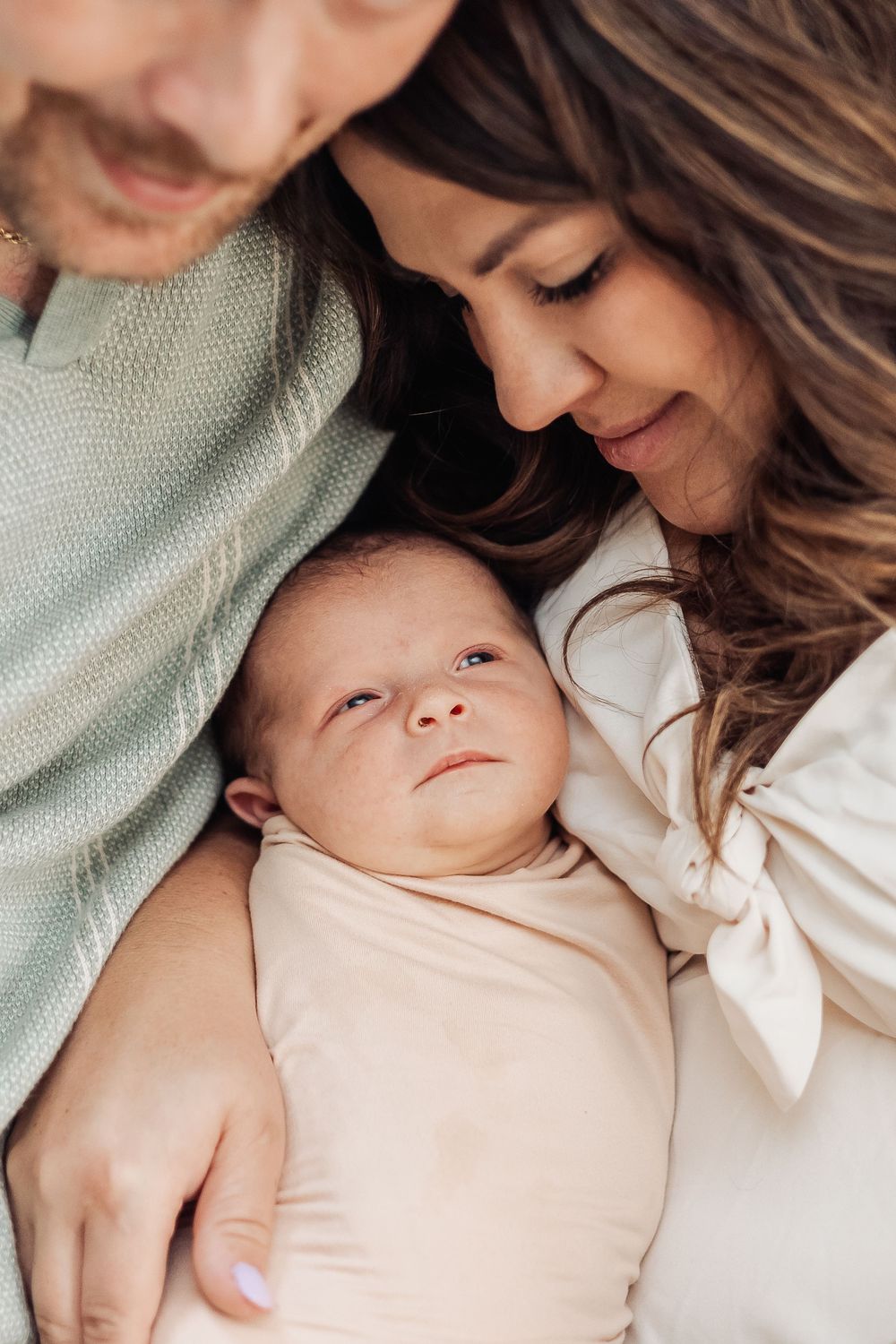 A tender family moment captured in soft lighting as parents lovingly embrace their newborn baby.