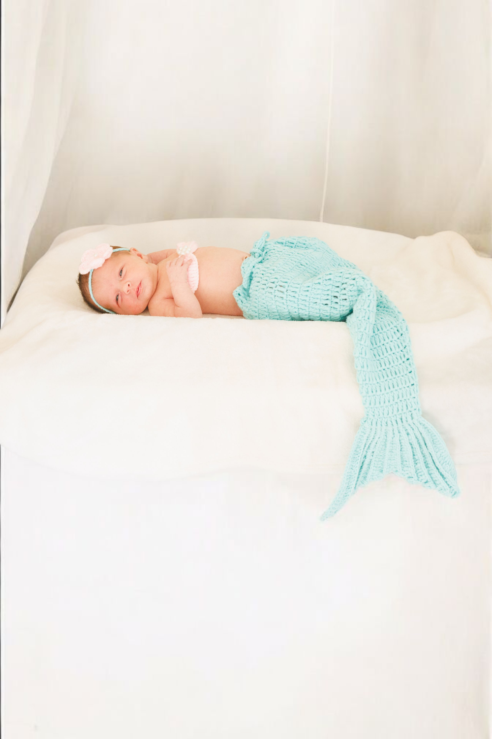 Baby sleeping on white bedding wearing a handmade knit turquoise mermaid tail costume.