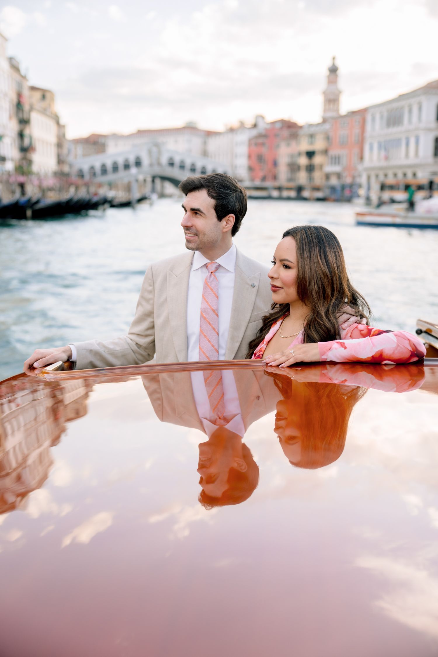 A couple enjoys a romantic gondola ride through the canals of Venice at sunset with historic buildings in the background.