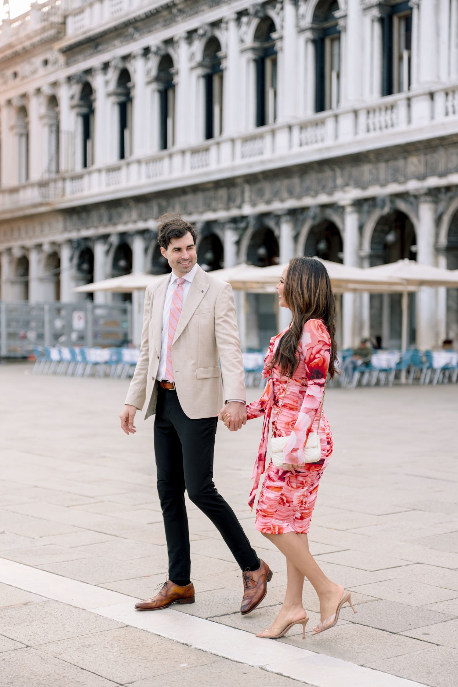 A stylish couple strolls along the historic Doge's Palace arcade in Venice's St. Mark's Square.