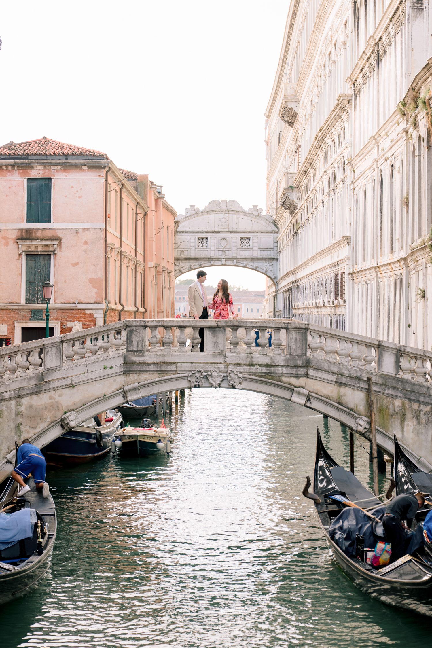 Romantic gondolas glide under stone bridges along a scenic Venice canal with historic buildings lining the waterway.