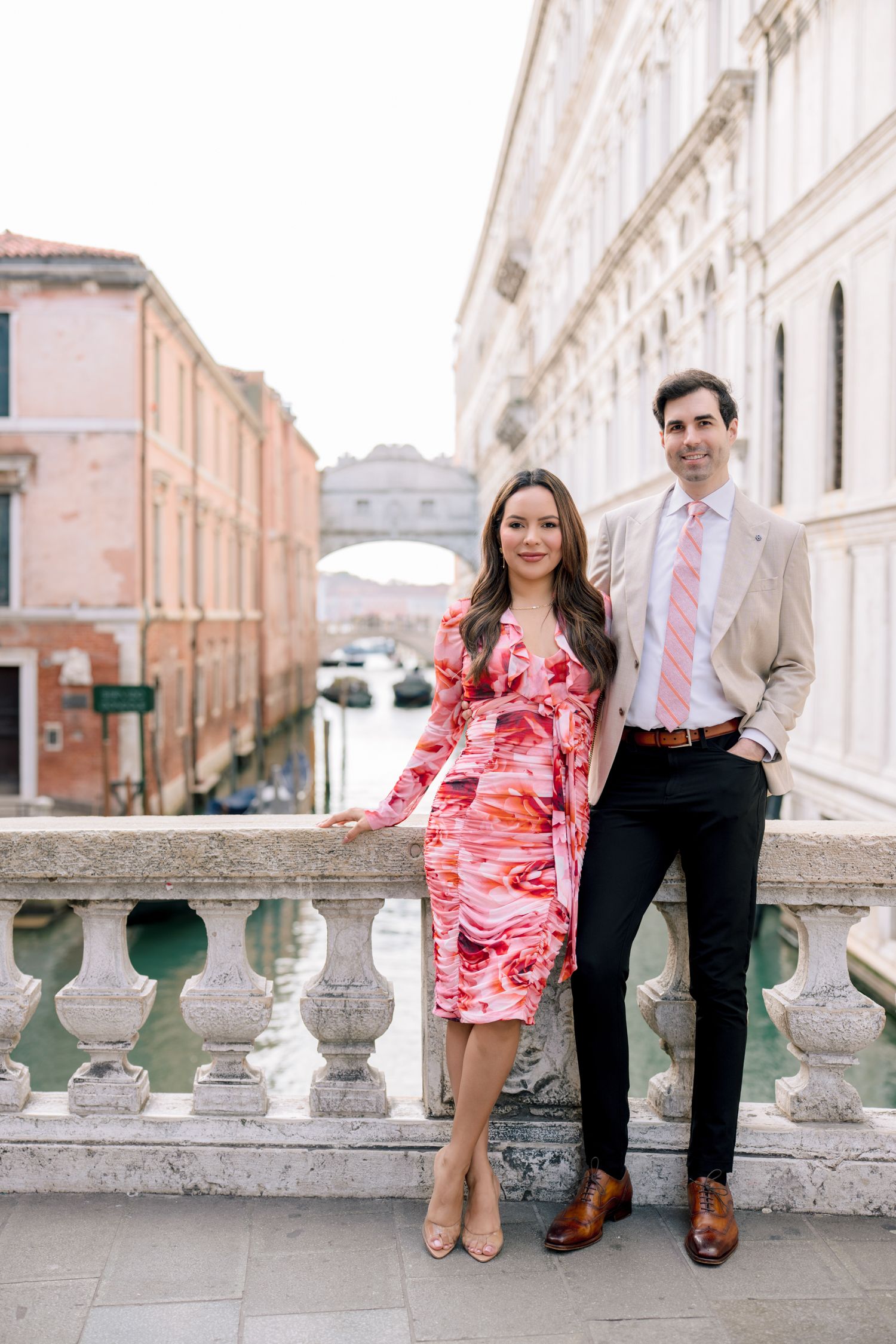A couple sits together on stone balustrades along a picturesque European street with historic architecture.