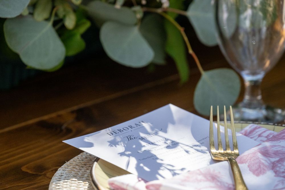Gold fork resting on a wedding menu card beside eucalyptus greenery on a wooden table.