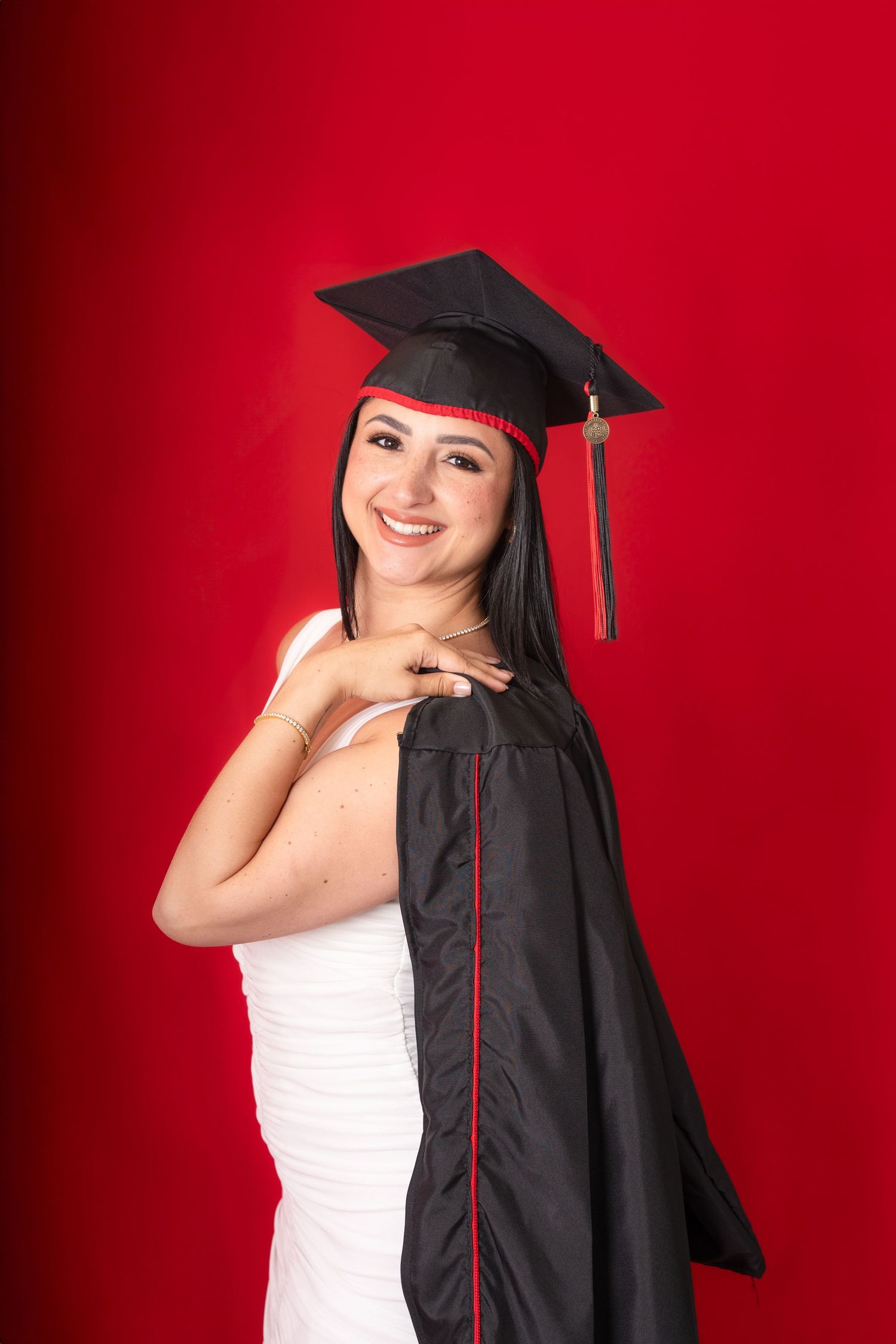 A graduate poses with a cap and gown on a red backdrop.