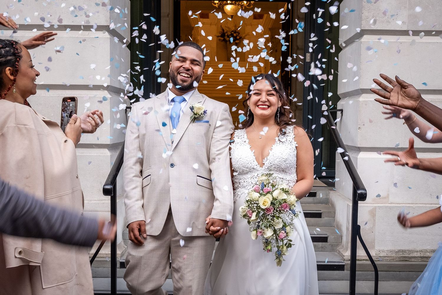 A couple in wedding attire walks together through a lush garden setting during their Islington ceremony.