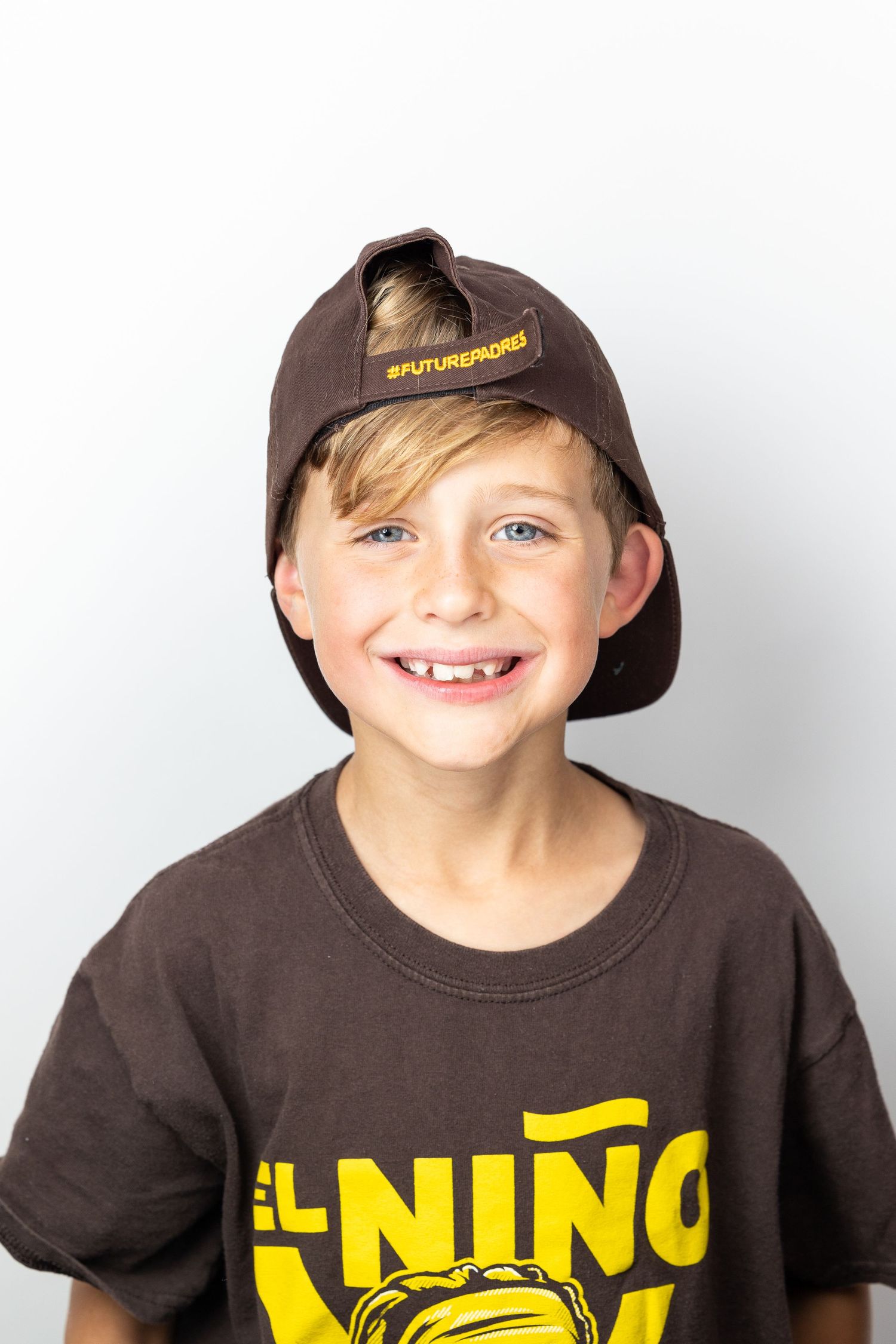 Happy young boy in brown cap and El Nino shirt smiles against white background.
