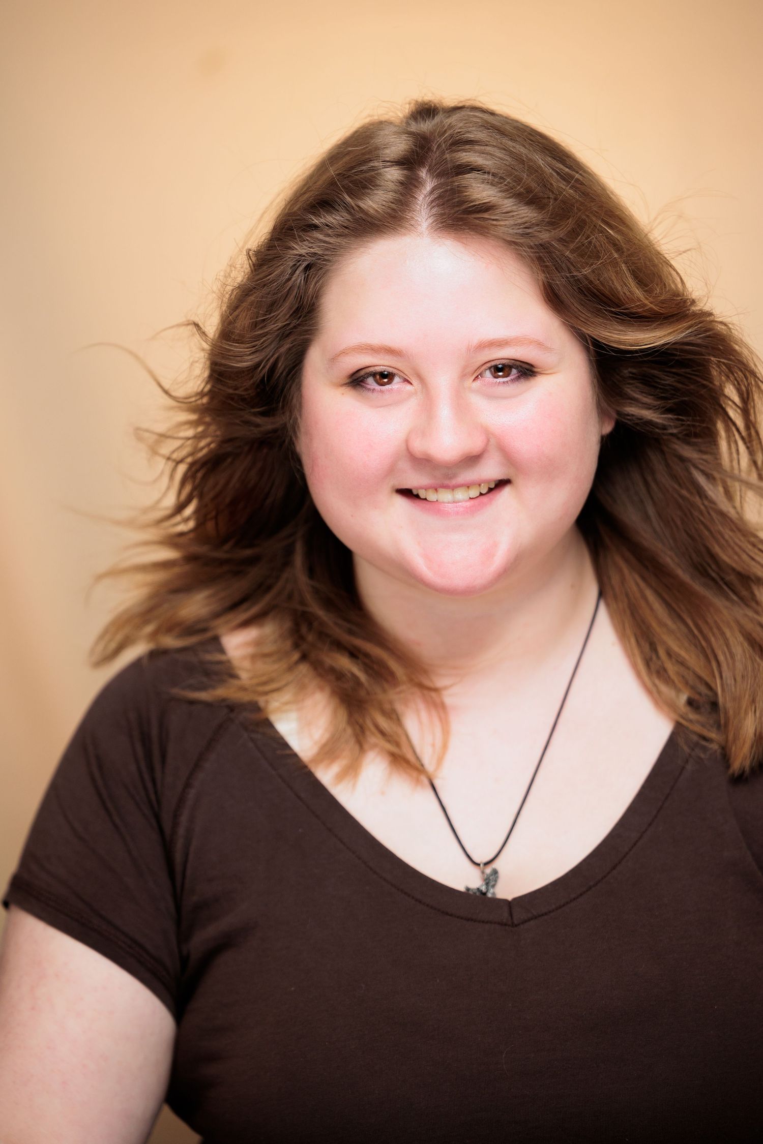 Young woman with brown hair smiles in black v-neck tee wearing pendant necklace.