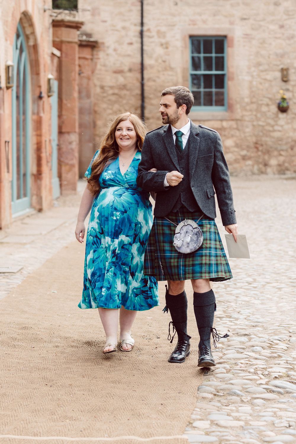 Close-up view of feet walking on cobblestone path showing traditional Scottish wedding attire and blue dress details.