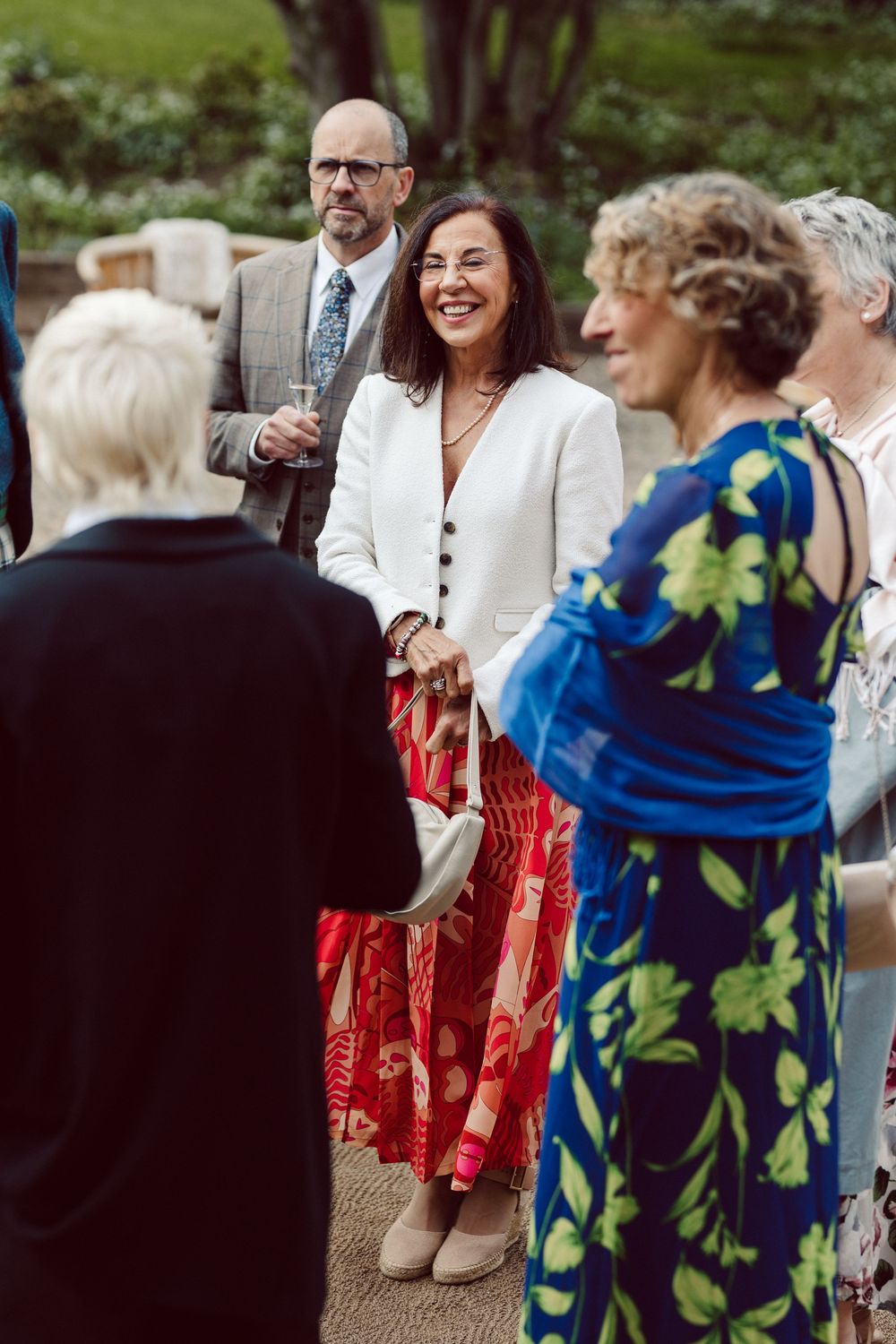 Wedding reception guests mingling outdoors in colorful summer attire with red dresses and floral prints.