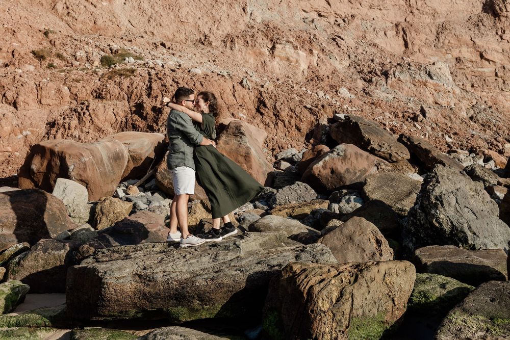 A woman standing on rocks near a body of water, surrounded by a natural, rugged landscape.