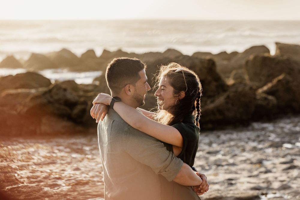 A couple embracing on a beach with a scenic ocean view in the background.