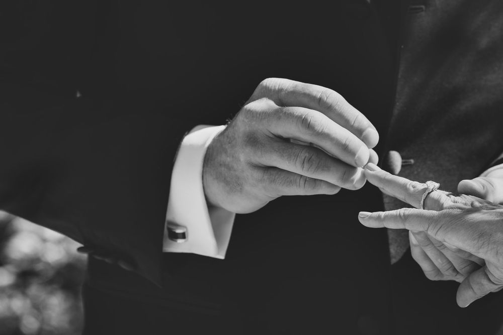 Black and white photo of a groom placing a wedding ring on his partner's finger during a ceremony.