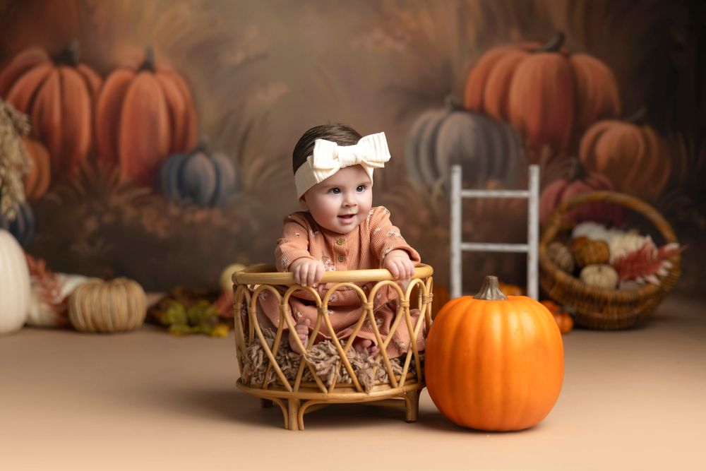 Baby girl in rust outfit sits in wicker basket surrounded by pumpkins and fall decor for autumn mini session.