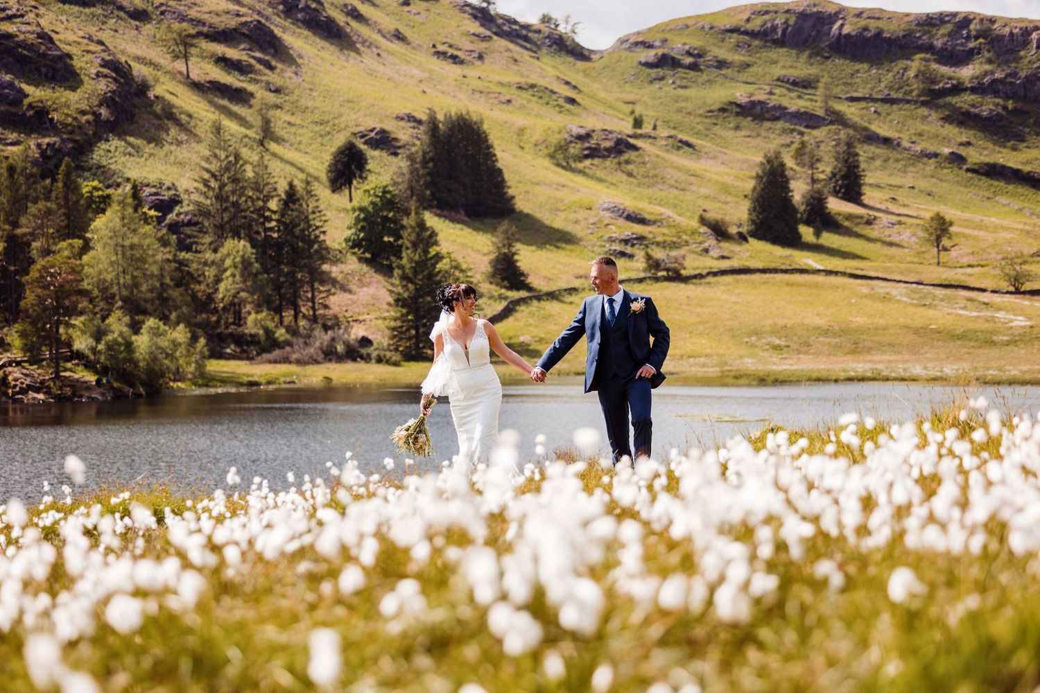 Bride and groom walk hand in hand along a garden path lined with yellow daffodils on their wedding day.