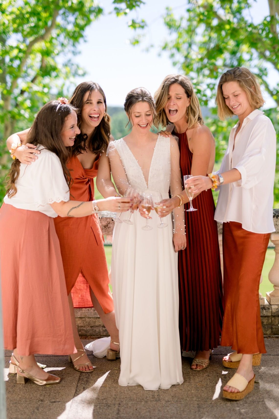 A group of women in white and rust-colored dresses laugh together while looking down at their feet in a candid photo series.