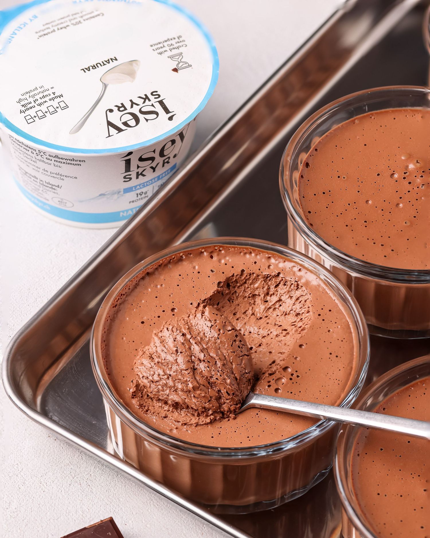 A spoon scoops creamy chocolate mousse from a glass bowl showing its smooth and airy texture.