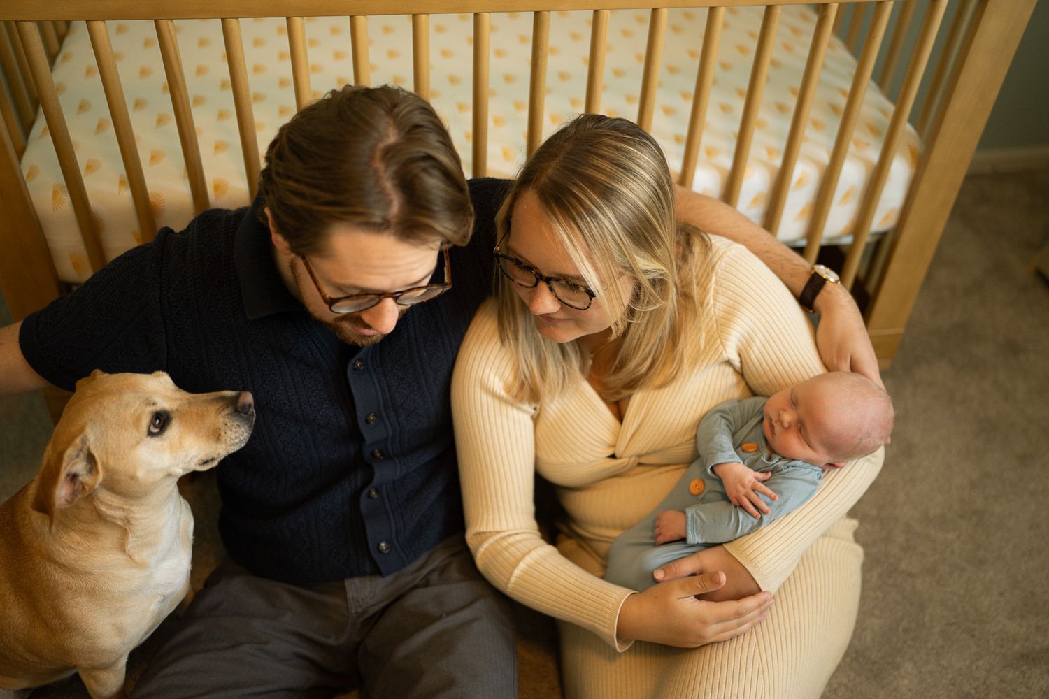 A couple sits on the floor with their baby and golden retriever, creating a cozy family moment at home.
