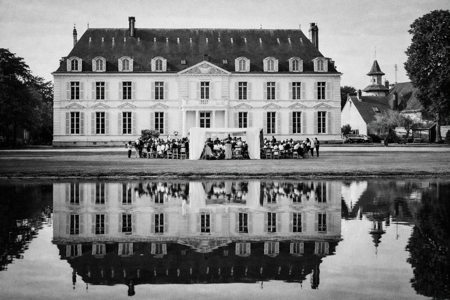 French chateau wedding ceremony set in front of chateau barthelemy with outdoor ceremony and reflection over pond in timeless black & white