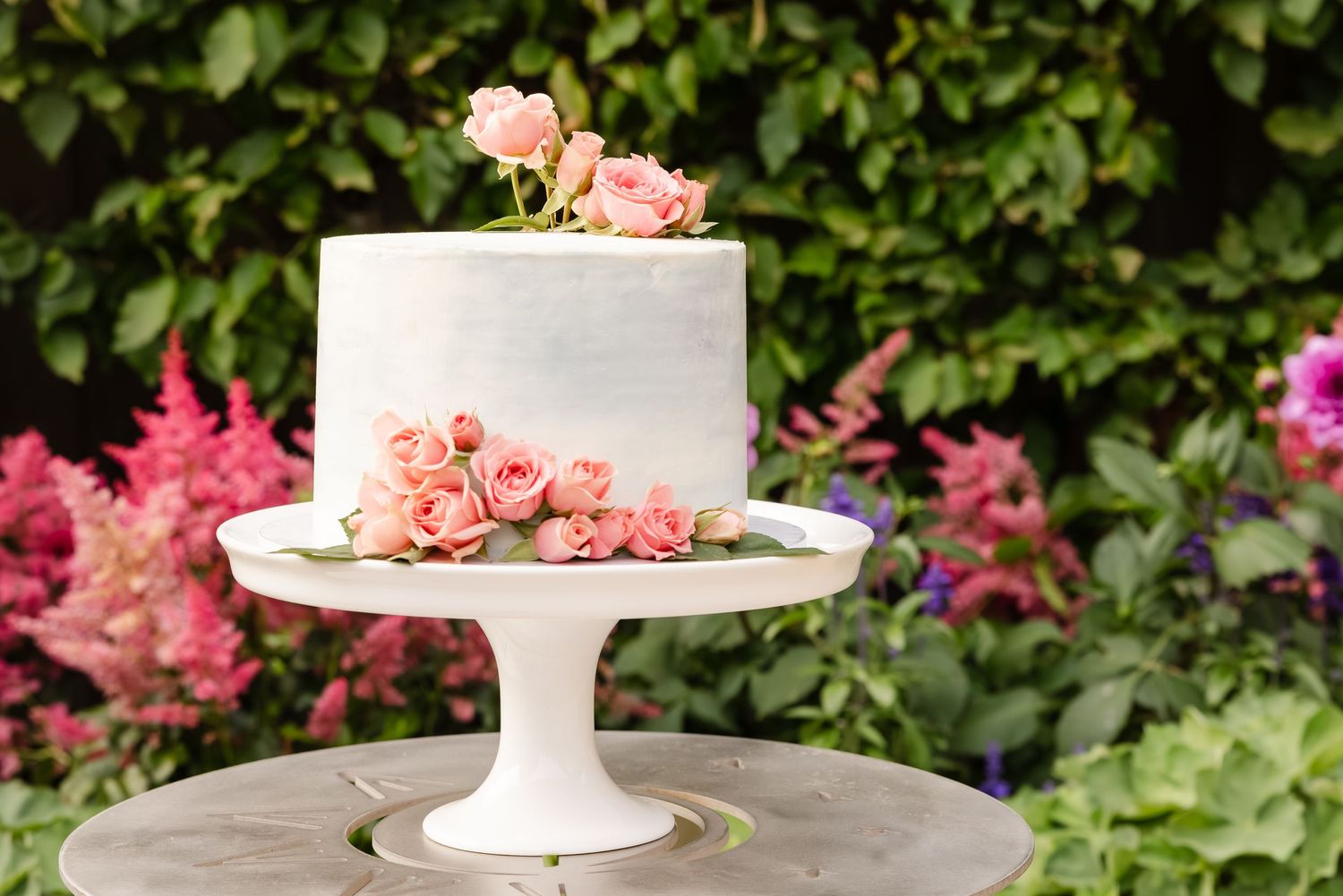 Pink floral arrangements in white pedestal vases create an elegant garden party display with lush greenery backdrop.