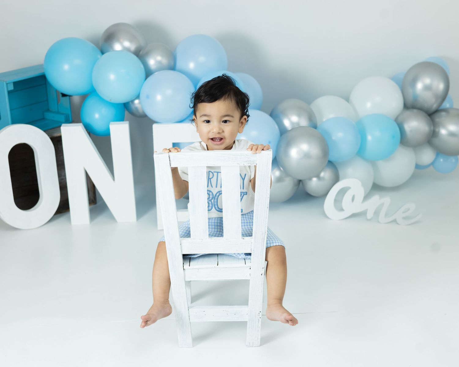 Baby crawls under blue and silver balloon arch during first birthday photo session.