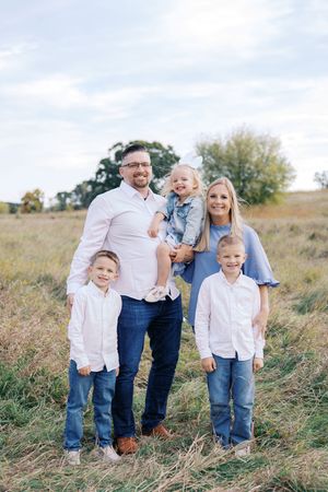 A family of five poses together in a grassy field on an autumn afternoon wearing coordinated casual outfits.