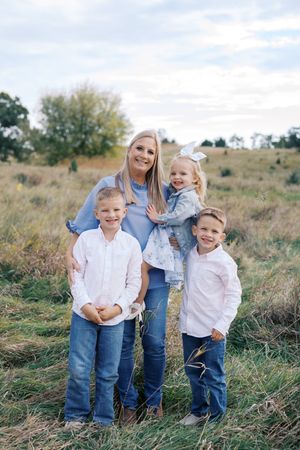 A group of four poses together in a rustic outdoor setting with tall grass and blue sky.