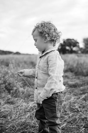 Black and white portrait of a toddler exploring tall grass in a field.