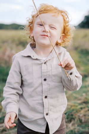 A toddler in a light colored shirt plays with a stick outdoors.