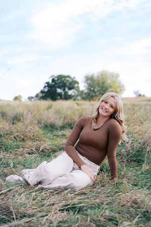 Woman in brown sweater relaxing in autumn field during sunset.