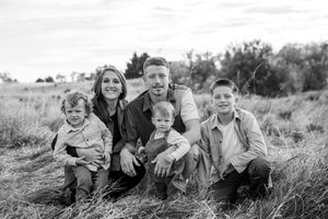 Family relaxing together in a grassy meadow during an outdoor black and white photo session.
