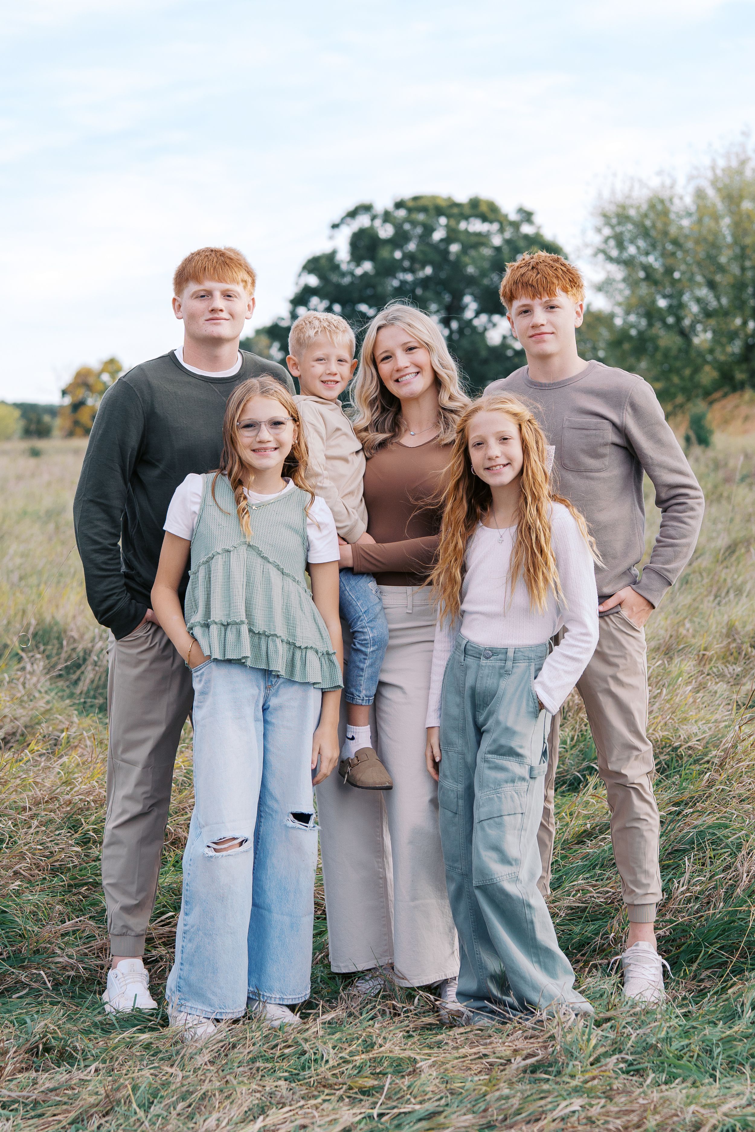 Family group wearing coordinated neutral tones poses casually together on a grassy hillside during golden hour.