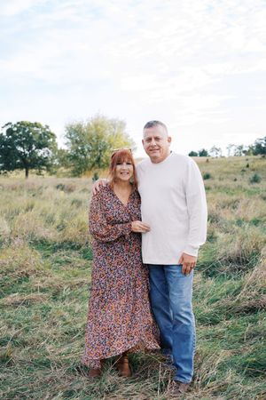 A couple poses together in a grassy field during an autumn photoshoot.