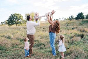 A joyful family plays together in a grassy field during golden hour.