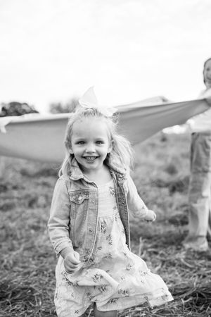 A black and white portrait of a child playing in a grassy field wearing a denim jacket.