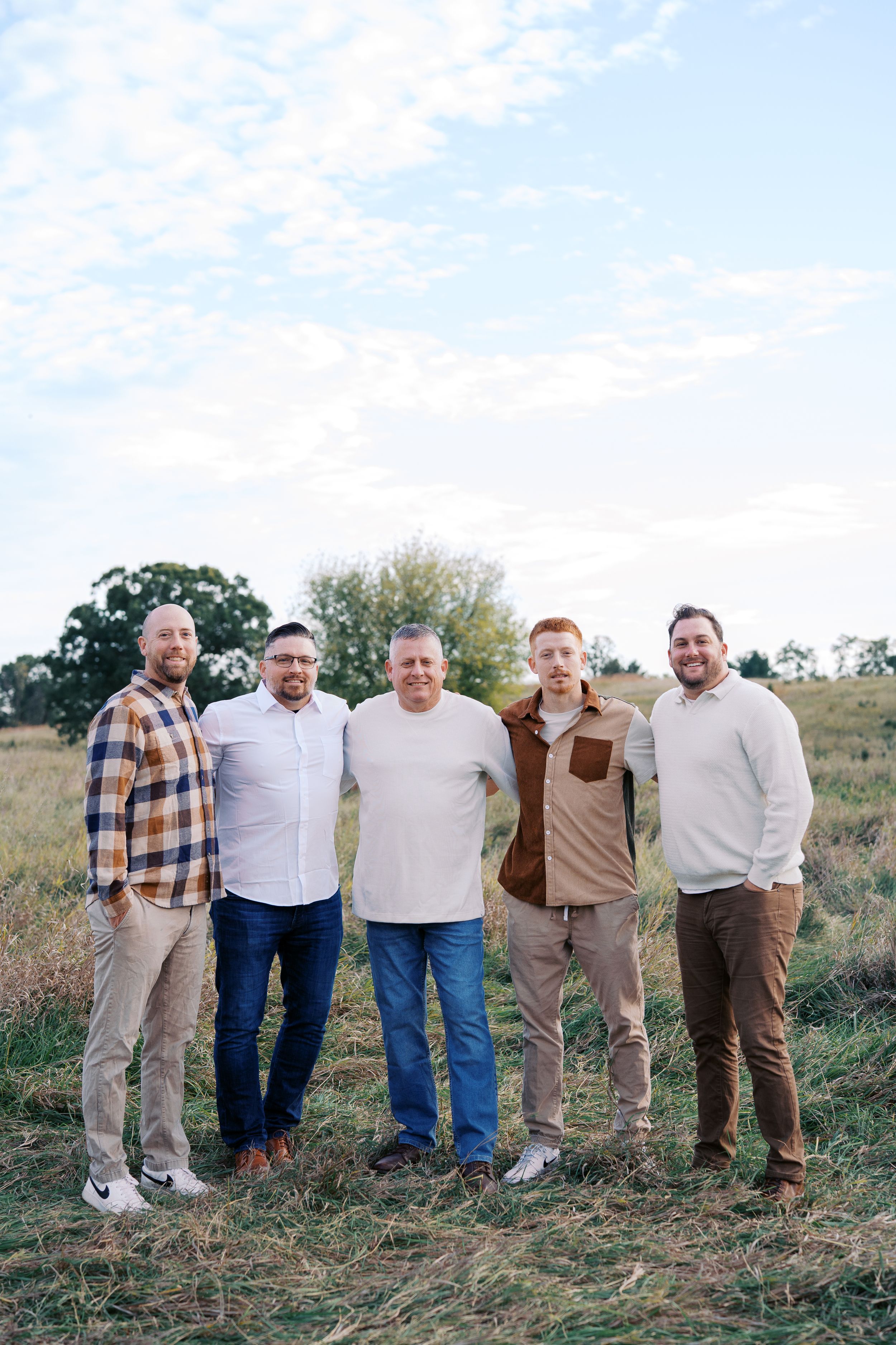 A group poses together on a hillside wearing coordinated casual outfits in earth tones.