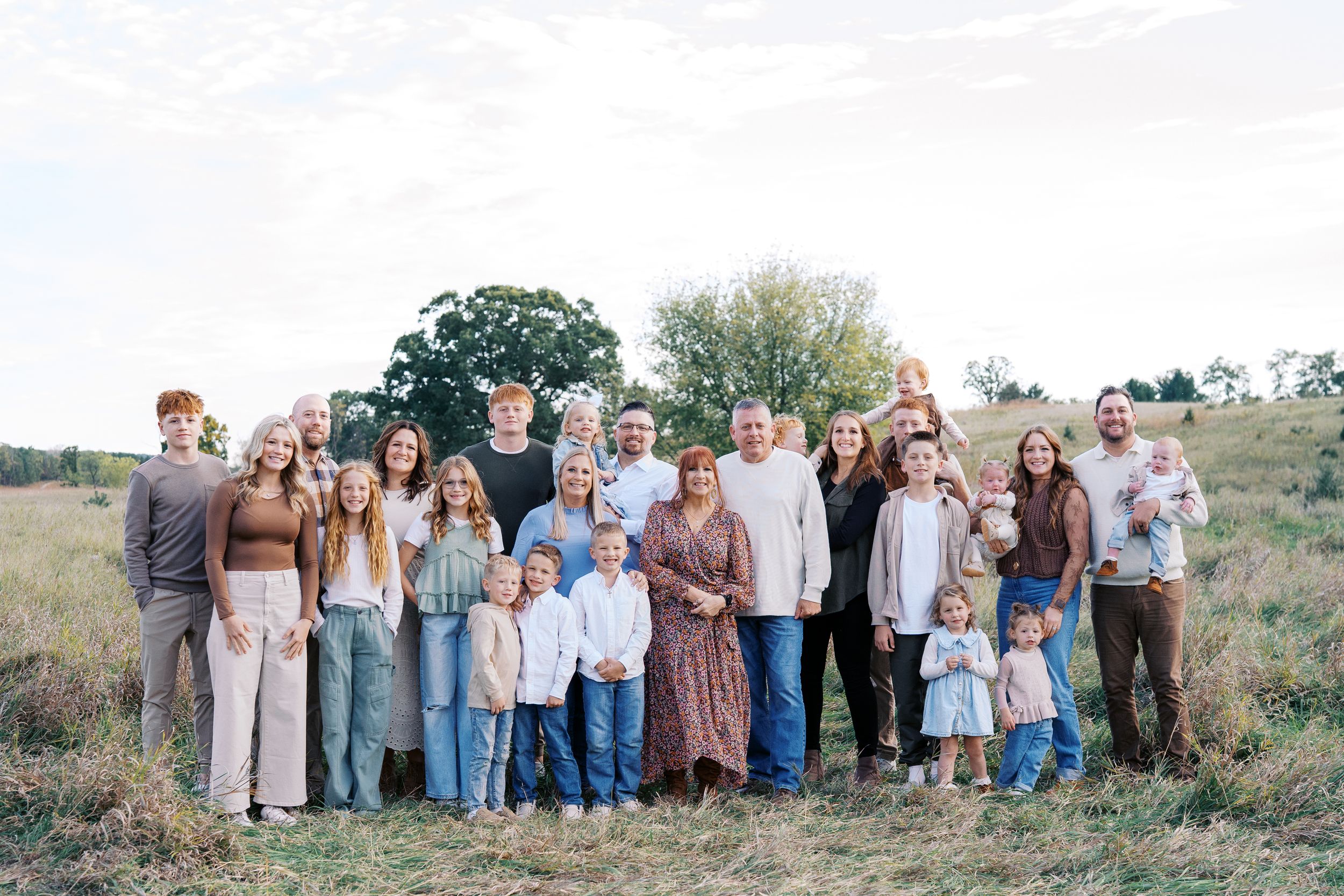 Large extended family group poses together outdoors in coordinated outfits against a natural landscape backdrop.