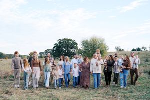 A large group of people stand together in a line across a scenic outdoor field.