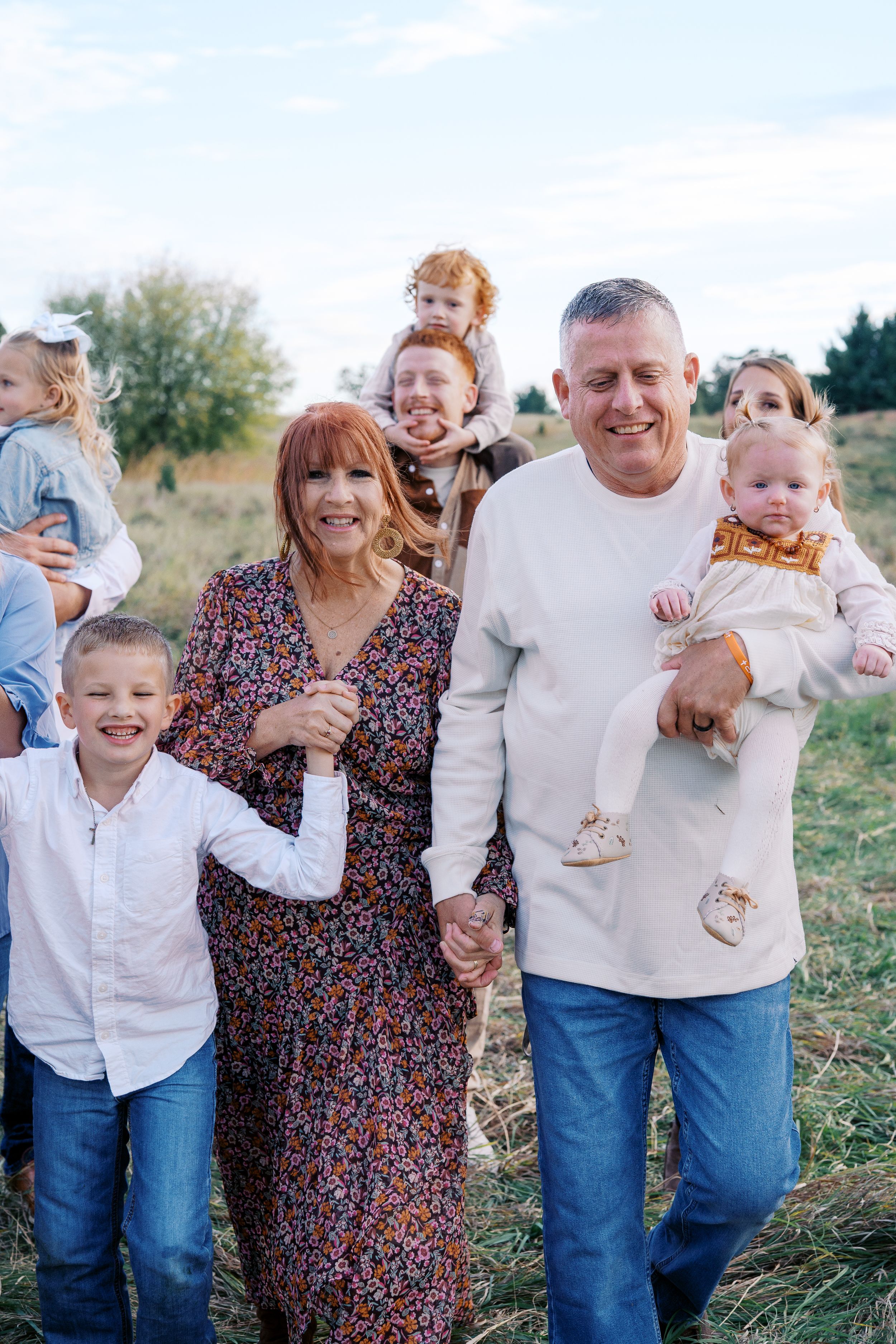 A family laughs and plays together in a grassy field during an outdoor photo session.