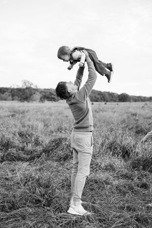 A silhouette of someone playing with a child, lifting them up in the air against a bright sky.