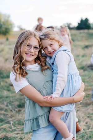 Two children share a sweet embrace while smiling and laughing together outdoors.