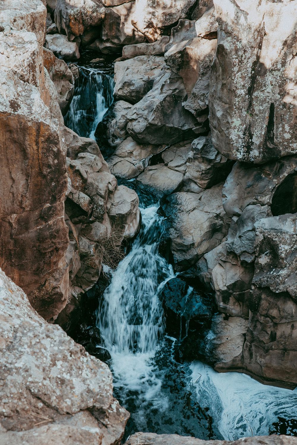 Water cascading down rocky canyon walls into a rushing stream below, natural waterfall landscape photography.