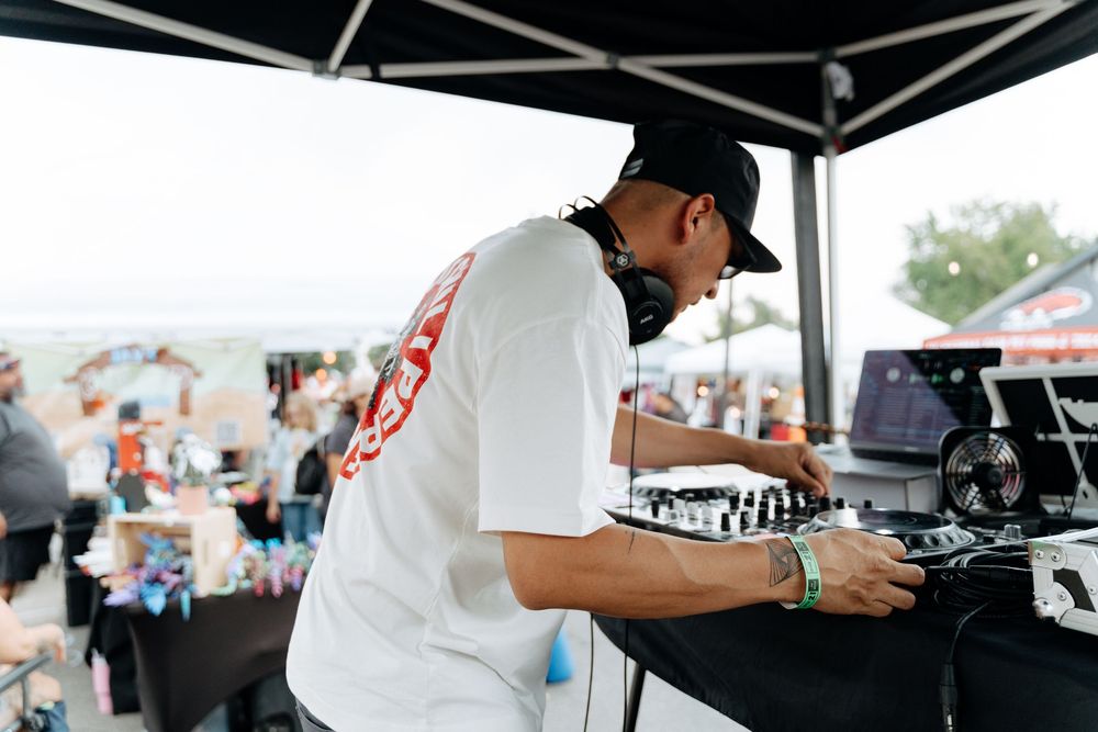DJ performing at an outdoor event with professional equipment under a black tent canopy.
