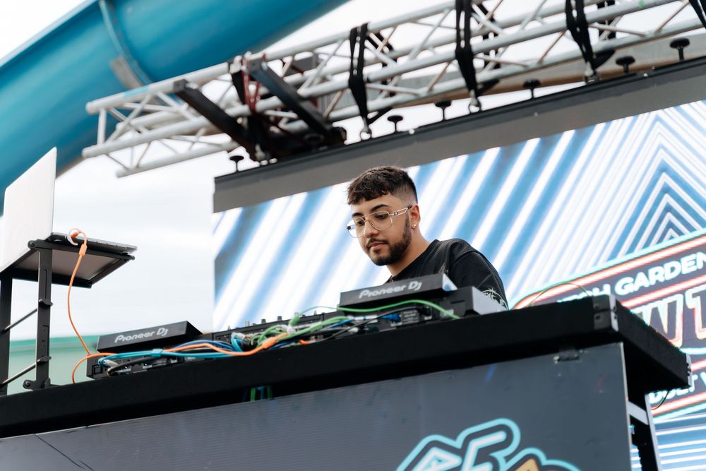 DJ performs on stage with professional equipment and turntables at a music event with blue lighting effects.