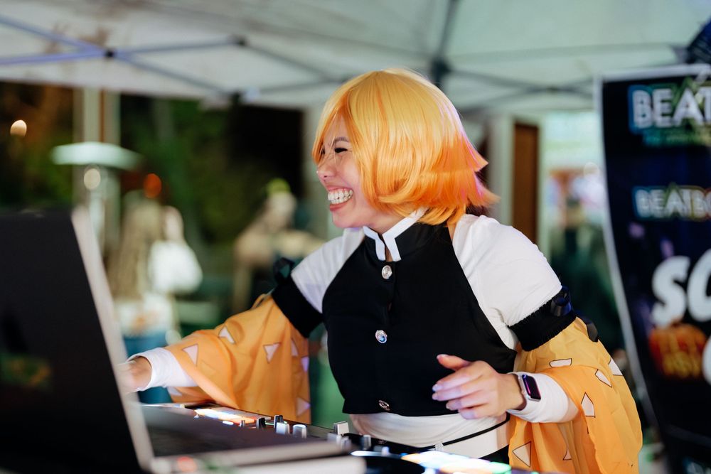 A person in a bright orange wig and black outfit serves beverages at an outdoor event.