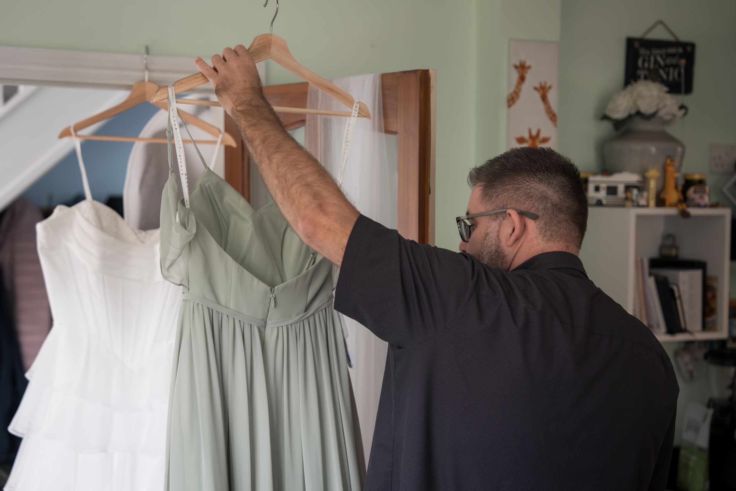 A row of wedding dresses hanging on wooden hangers in a bridal boutique with soft green walls.