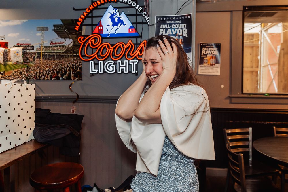 Woman laughing joyfully at a bar with a glowing Coors Light neon sign in the background.