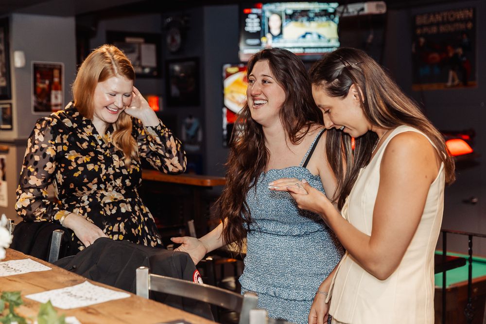 Three women laughing together at a bar counter, enjoying a fun social gathering in a casual restaurant setting.