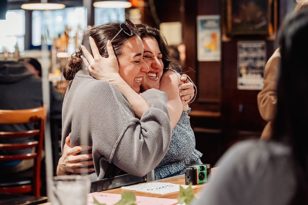 Two women sharing a warm embrace and smiling in a cozy restaurant setting.