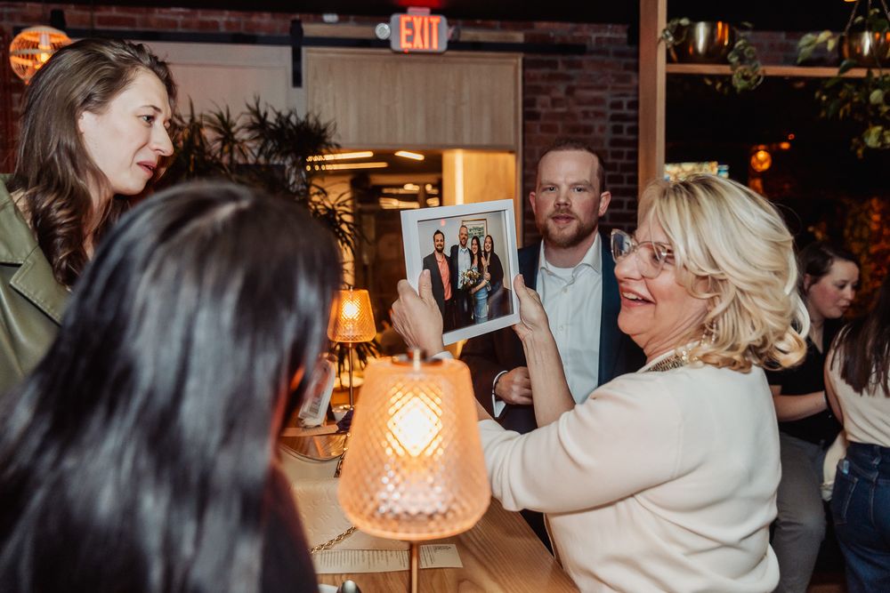 Woman proudly displays a framed family photo to guests at a social gathering.