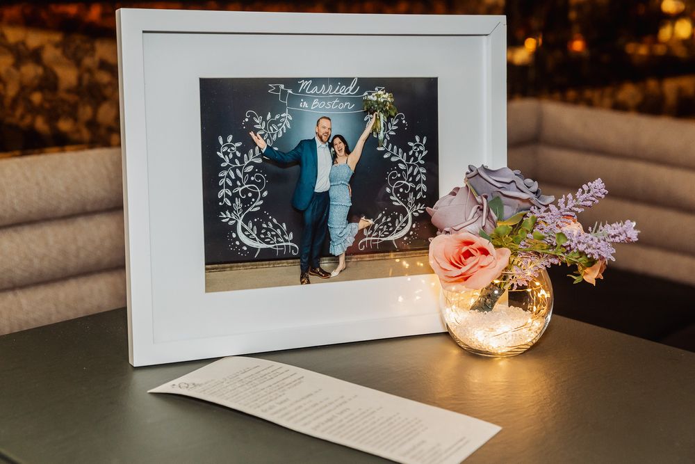 Framed wedding photo with floral decor and a glowing vase of pink and purple flowers on a table.